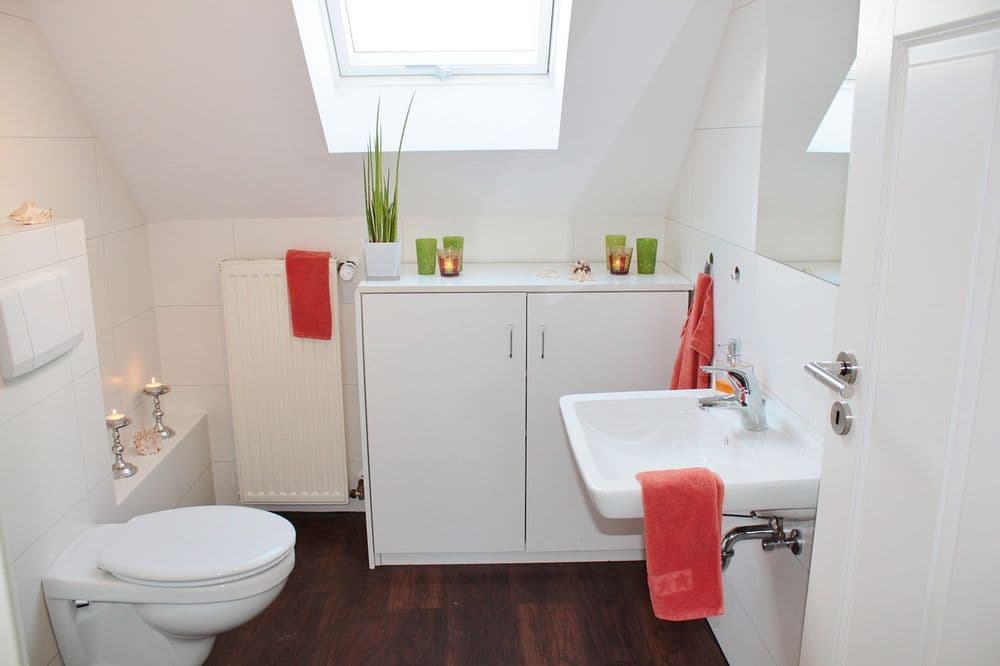 Modern attic bathroom featuring a white sink, toilet, and decorative candles on the counter.