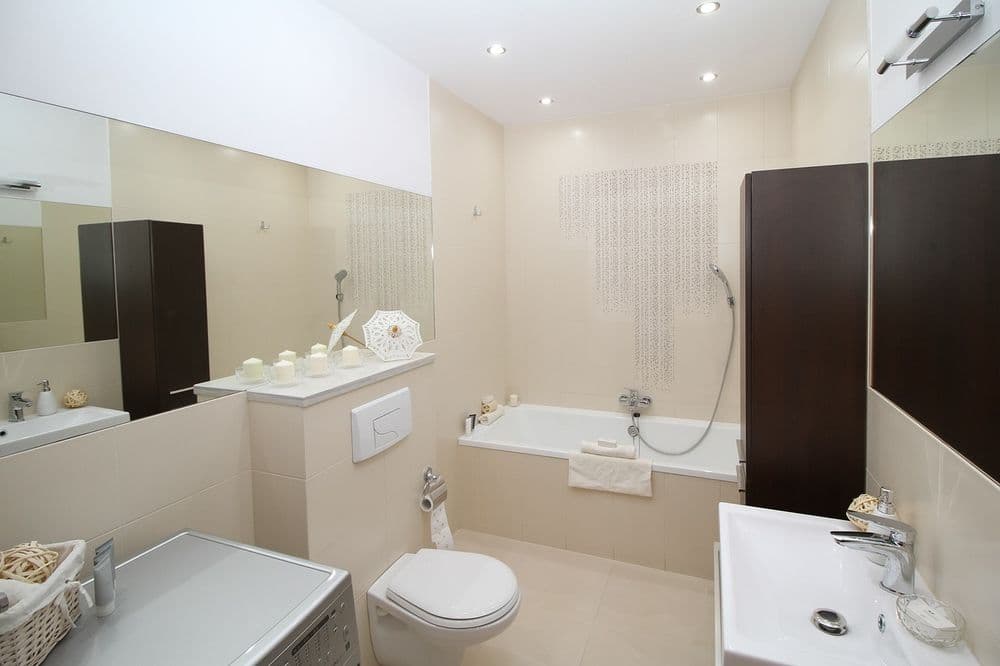 Modern bathroom with bathtub, toilet, sink, and stylish neutral decor. Bright lighting accents.