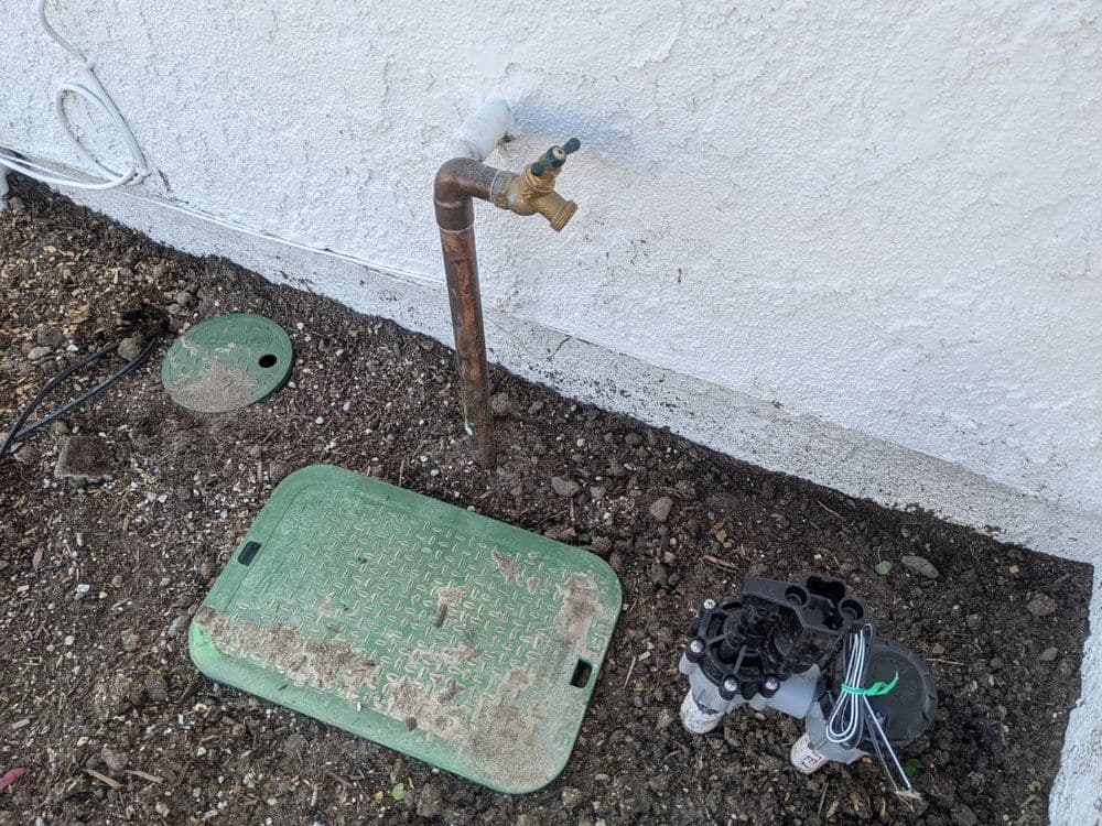 Water main shutoff valve installation next to control system on exterior wall.