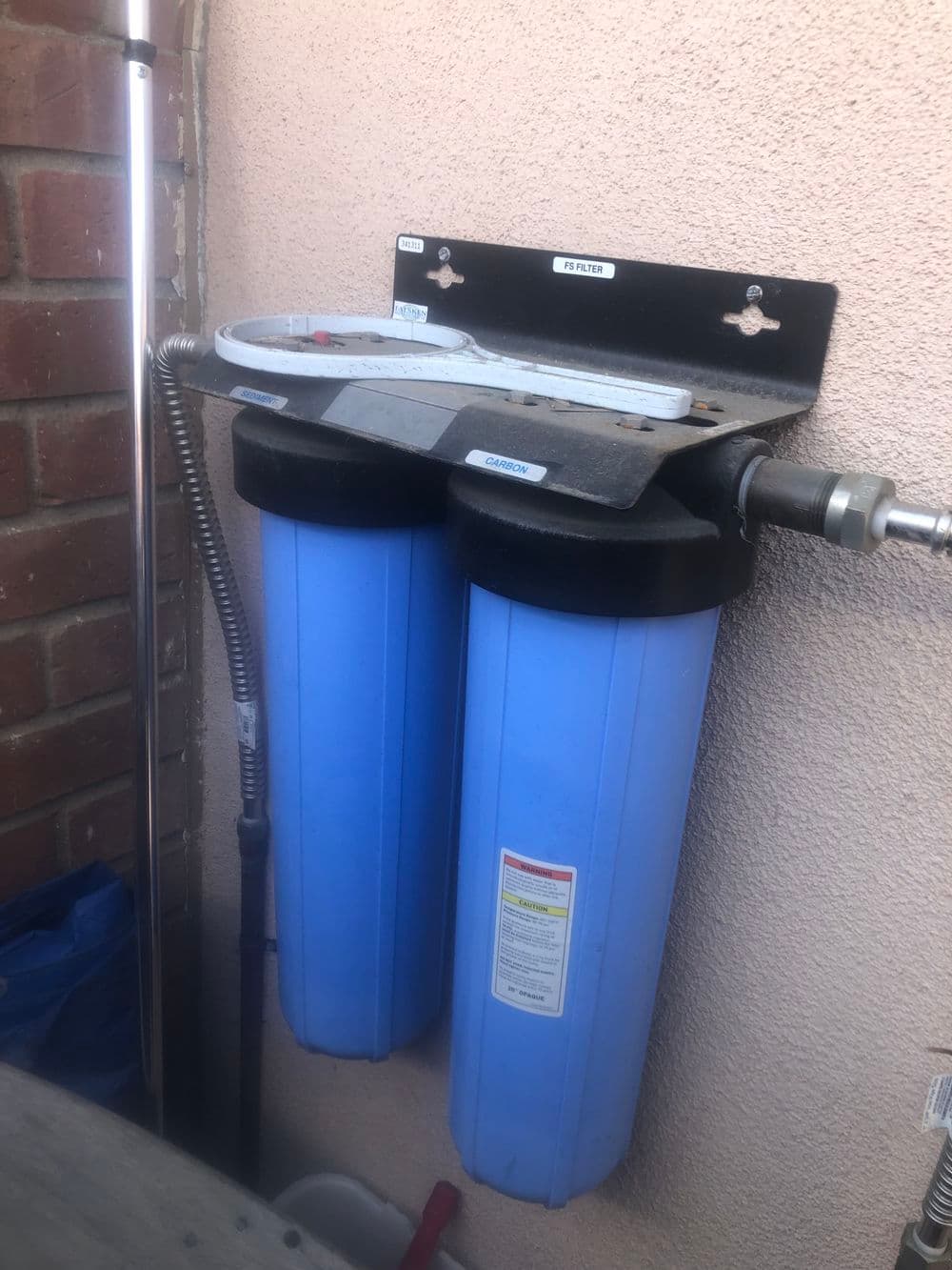 Blue water filtration system mounted on a wall, featuring dual filter cartridges.