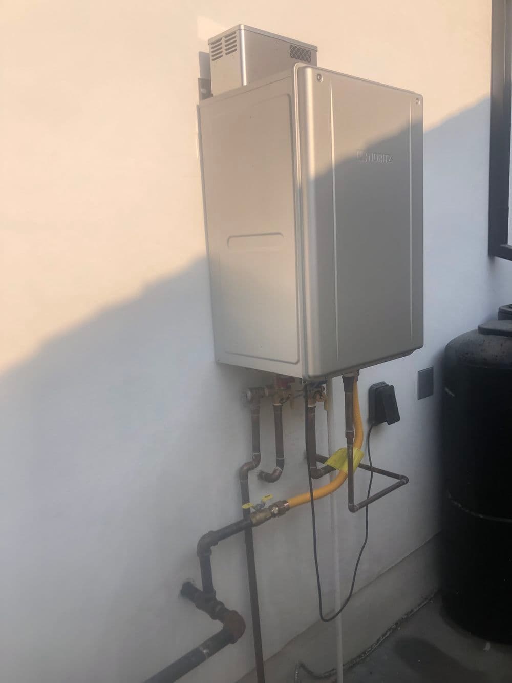 Tankless water heater mounted on wall with pipes and connections, energy-efficient design.