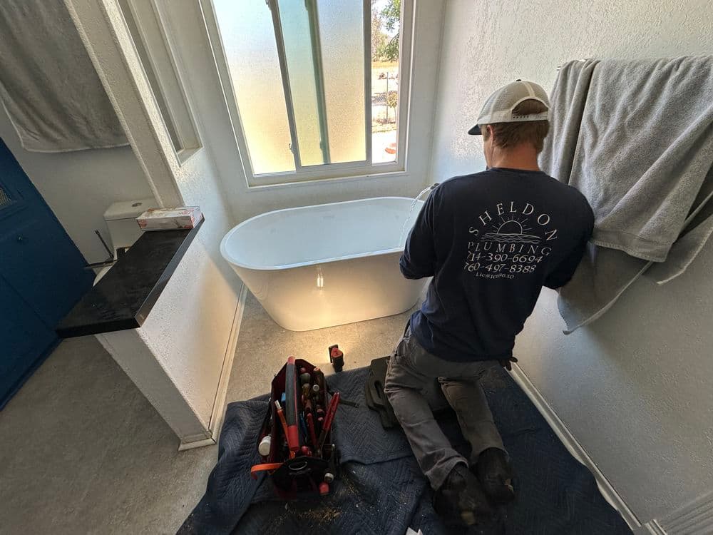 Plumber installing a modern freestanding bathtub in a bright, renovated bathroom.