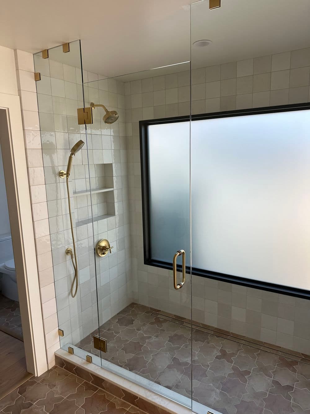 Modern glass shower with gold fixtures and frosted window in stylish bathroom interior.
