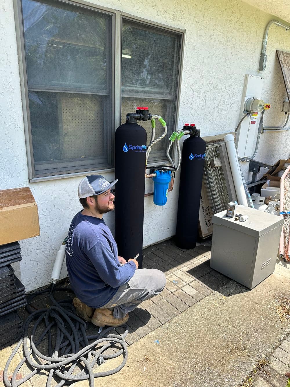 Technician installing SpringWell water filtration system outside a home.