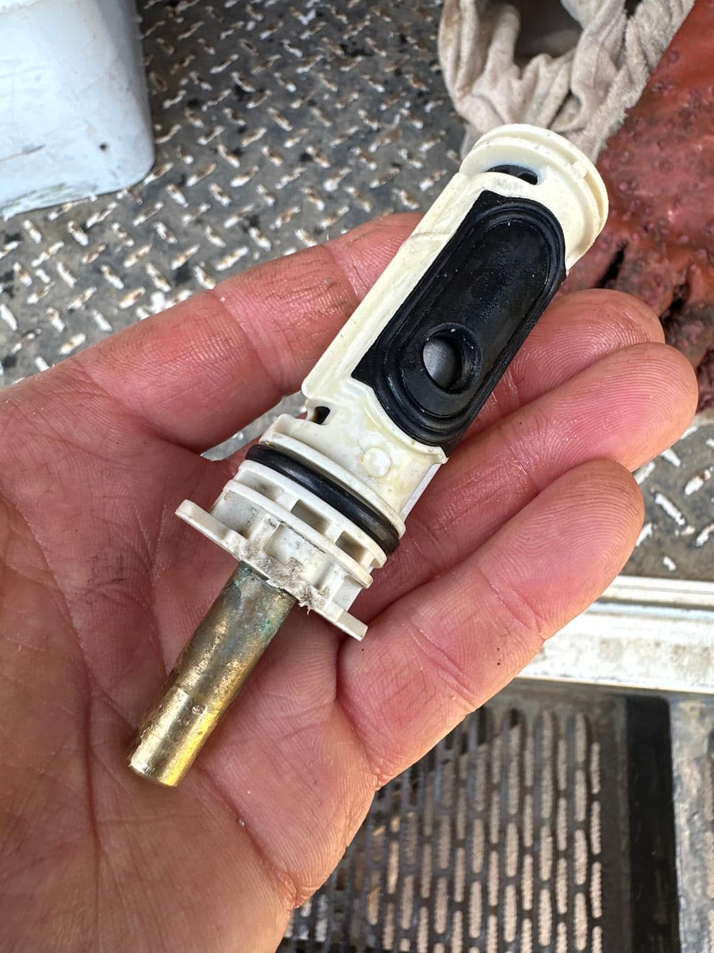 Hand holding a white and black mechanical valve component with a metal shaft.
