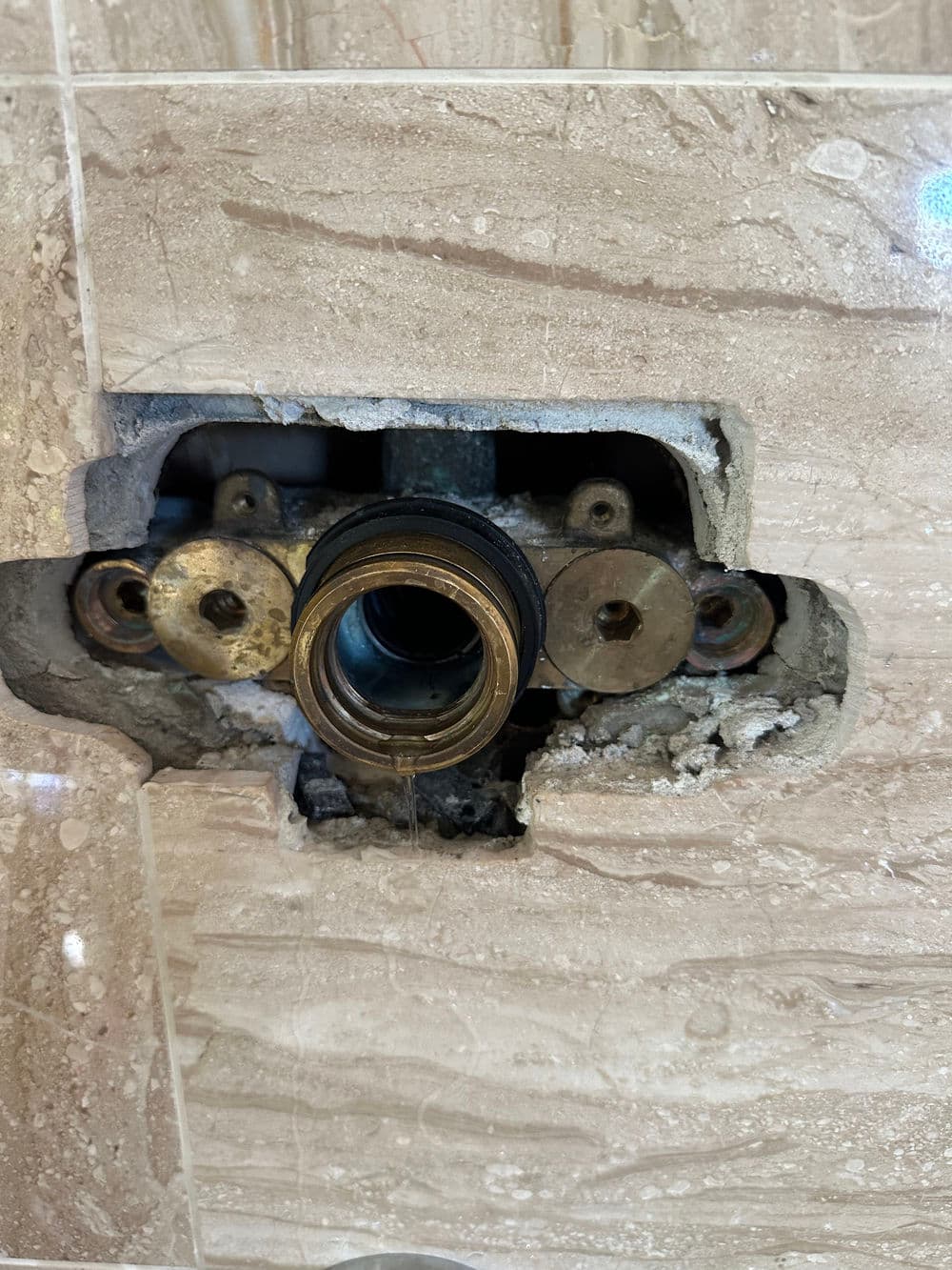 Exposed plumbing fixture in wall with metal fittings and marble tile background.